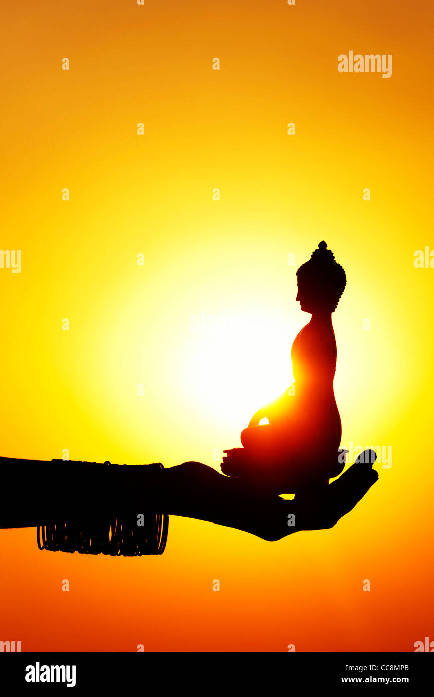 Indische Mädchen Hand mit einem Buddha Statue gegen die untergehende Sonne. Indien Stockfoto