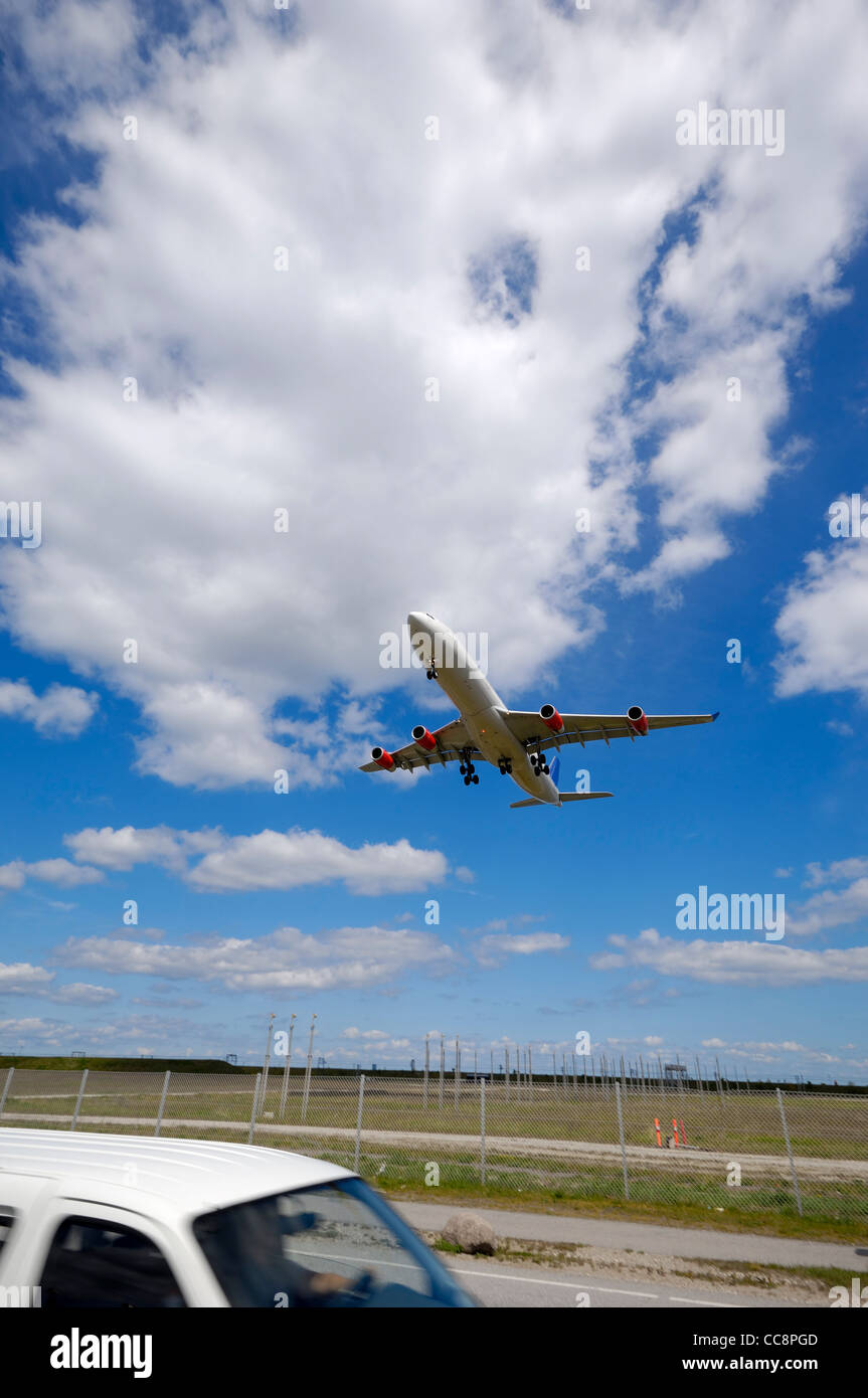 Große Engel Schuss eine Landung Flugzeug überqueren einer Straße mit einem Auto in Bewegung. Stockfoto