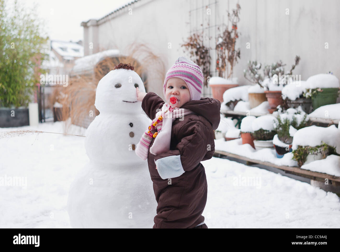 Babymädchen spielen mit Schneemann im Hinterhof Stockfoto