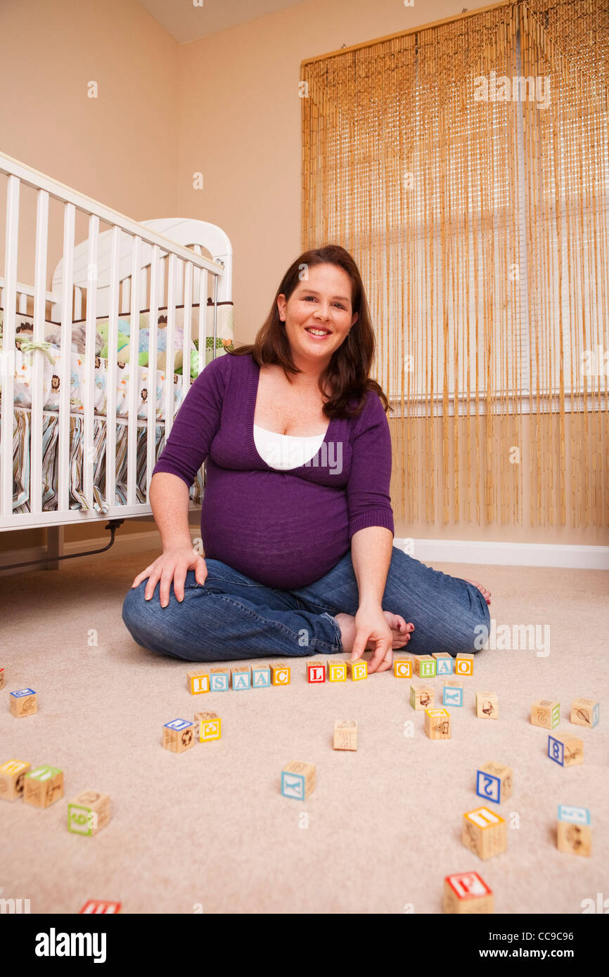 Schwangere Frau mit Bausteinen, sitzen am Boden neben der Krippe Stockfoto