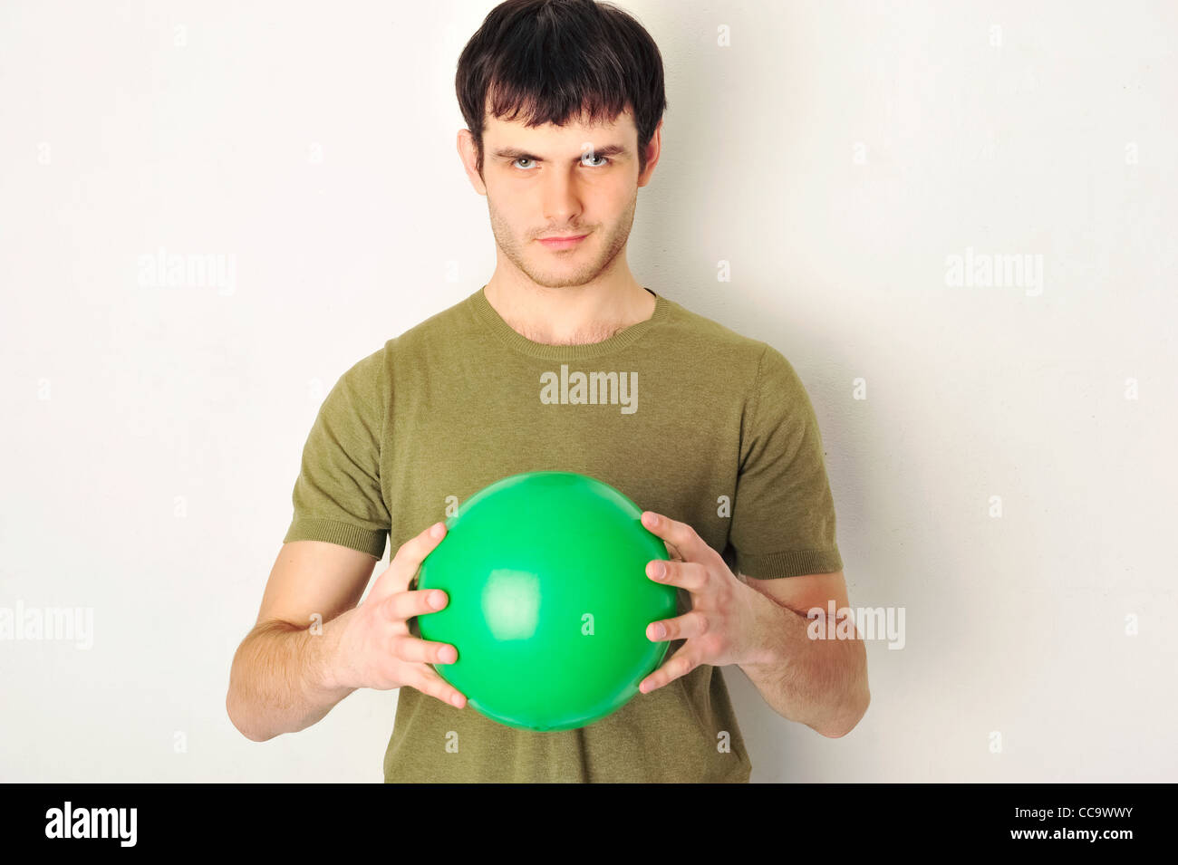 Porträt von gut aussehender Mann mit grünen Ball in seinen Armen. Stand in der Nähe der Wand in Turnhalle Stockfoto