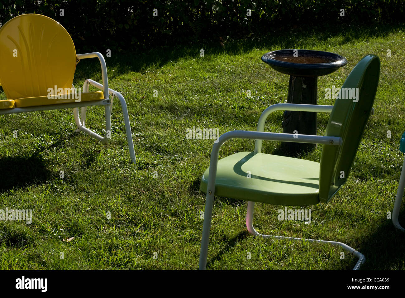 Leere Liegestühle und eine leere Vogelbad bevölkern eine Sommer-Wiese am Nachmittag. Stockfoto