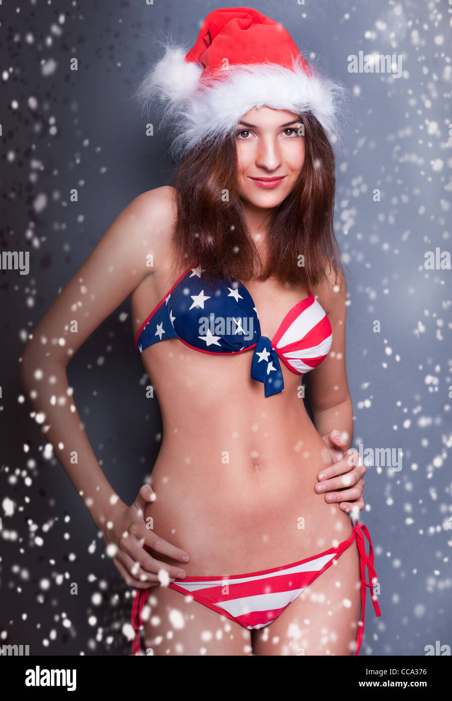 20-25 Jahre alte schöne Frau in Weihnachtsmütze und Badeanzug mit amerikanischen Flagge. Schneeflocken um sie herum Stockfoto