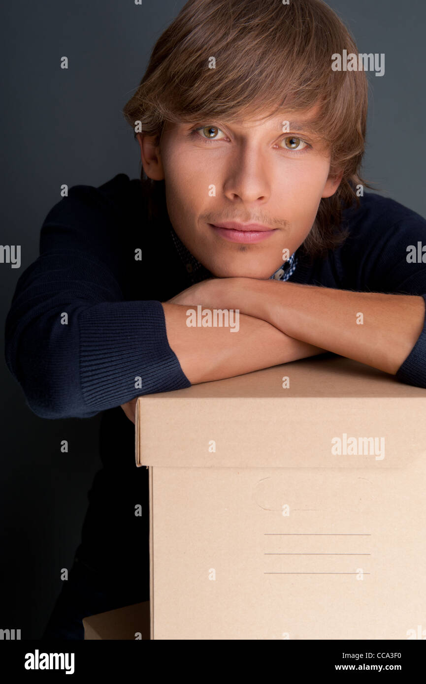 Porträt des jungen Mannes auf Box gegen graue Wand halten. Er ist neues Leben beginnen. Stockfoto