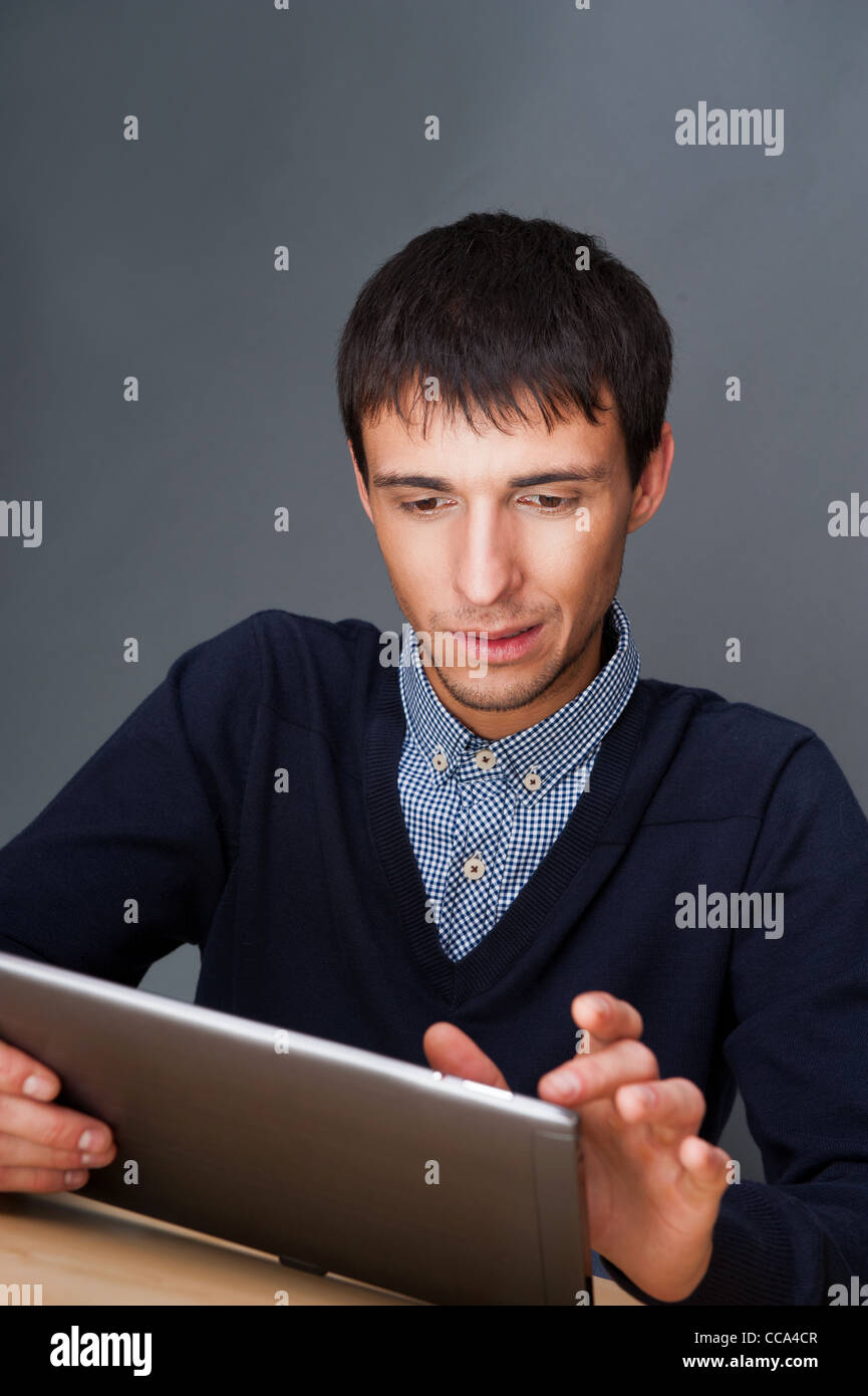 Nahaufnahme eines lächelnden Geschäft Jünglings sitzt in seinem Büro gegen graue Wand und mit seinem modernen TabletPC um sein Werk zu tun Stockfoto