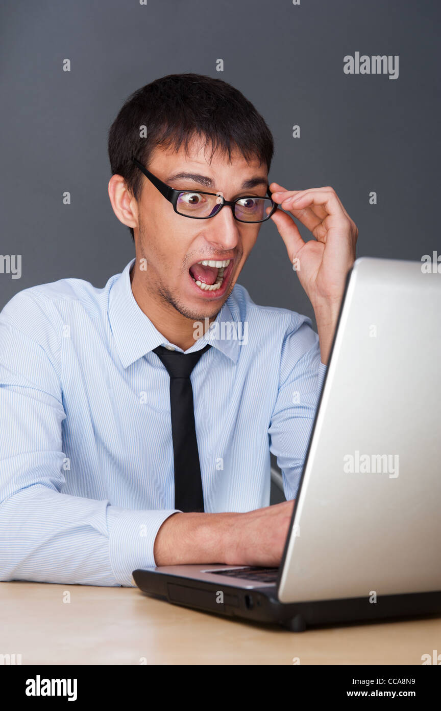 Attraktive junge Mann in seinem Büro mit einem Laptop arbeiten. Er ist schreien und sehr ausdrucksstark Stockfoto