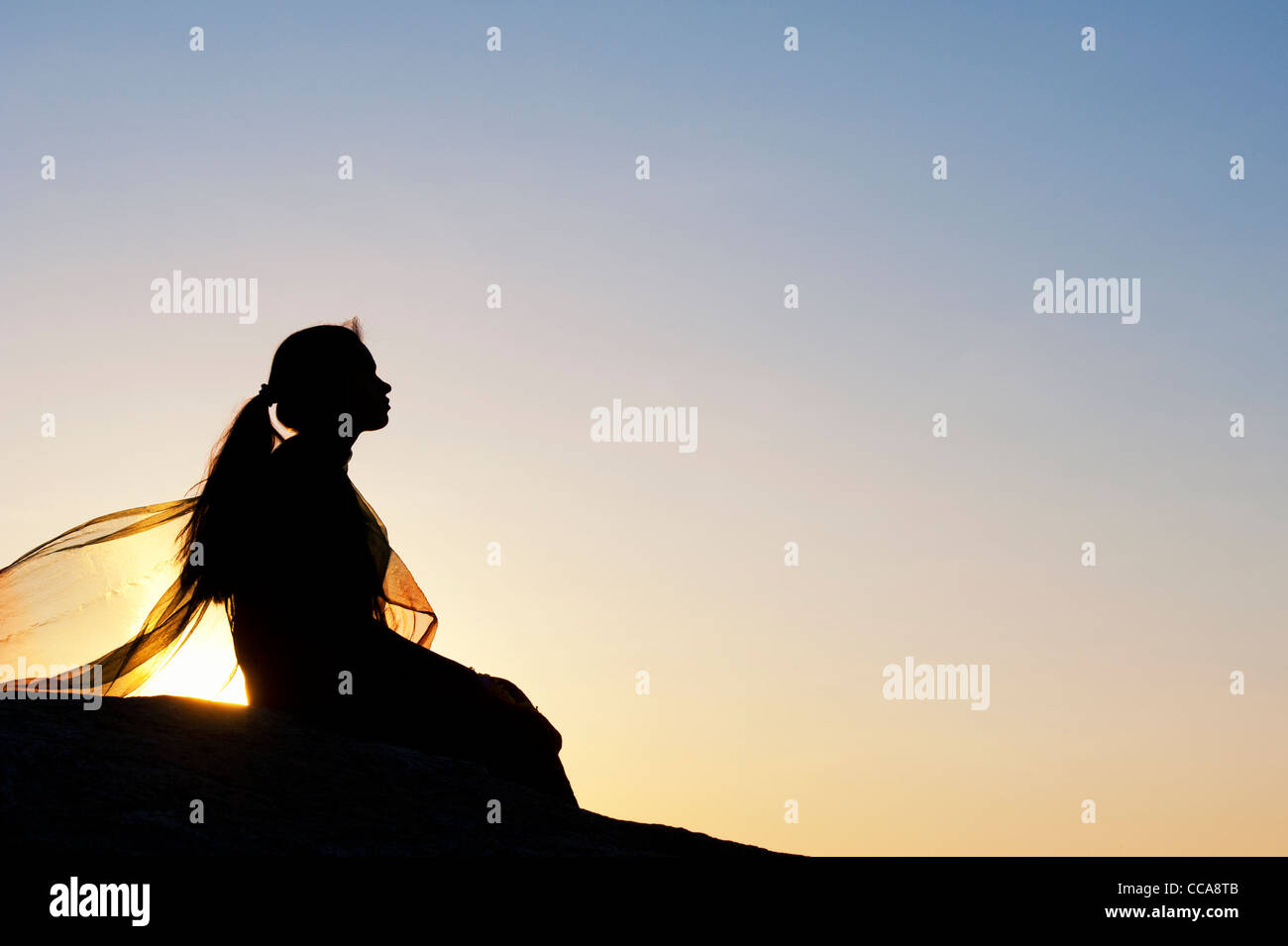 Indisches Mädchen ganz allein auf einem Stein saß bei Sonnenuntergang. Silhouette. Andhra Pradesh, Indien Stockfoto