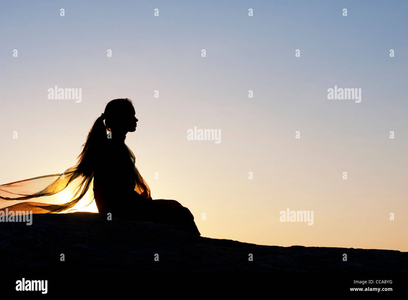 Indisches Mädchen ganz allein auf einem Stein saß bei Sonnenuntergang. Silhouette. Andhra Pradesh, Indien Stockfoto