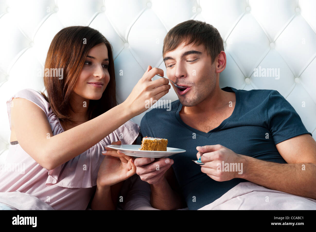 Porträt des glücklichen Paares im Bett liegend. Füttern ihren Freund mit Löffel leckeren Kuchen Mädchen Stockfoto