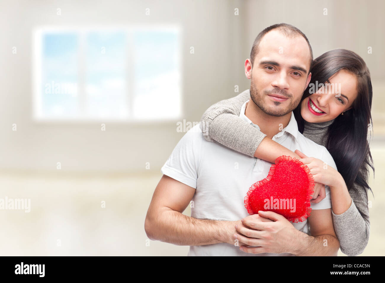 Porträt von junges Paar mit roten Herzen stehen in ihrem Zuhause und umarmen. Sie sind wirklich glücklich zusammen sein Stockfoto