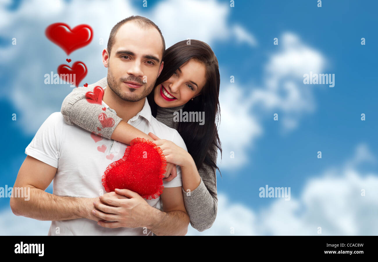 Junge Erwachsene Brautpaar mit roten Herz auf romantischen Hintergrund mit Himmel und Wolken, umarmen und lachen. Viele Exemplar Stockfoto