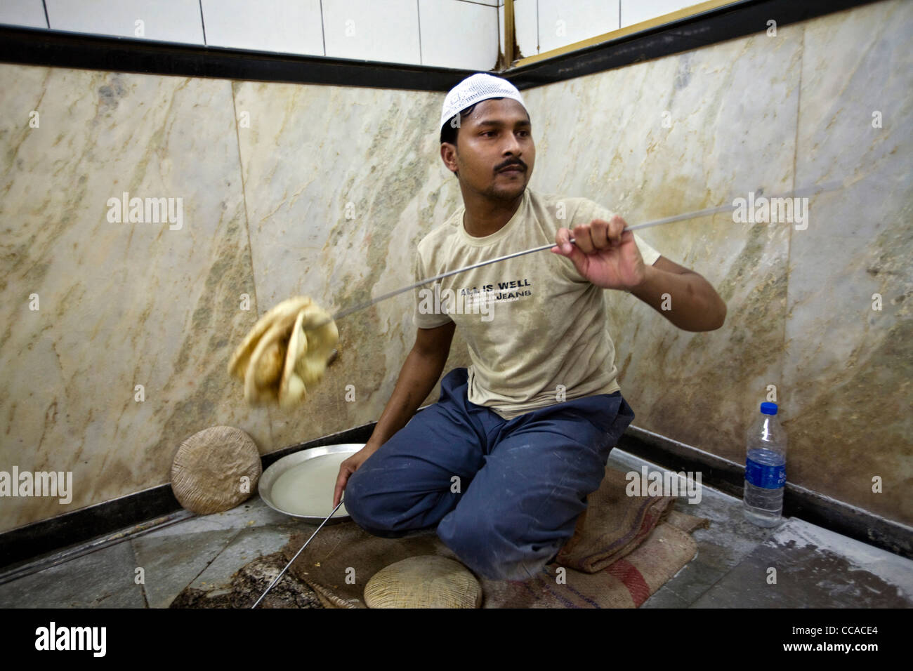 L M Rahman wirft frisches Naan Brot aus dem Tandoor-Ofen zu einem Kellner im Restaurant Karims, Delhi, Indien Stockfoto