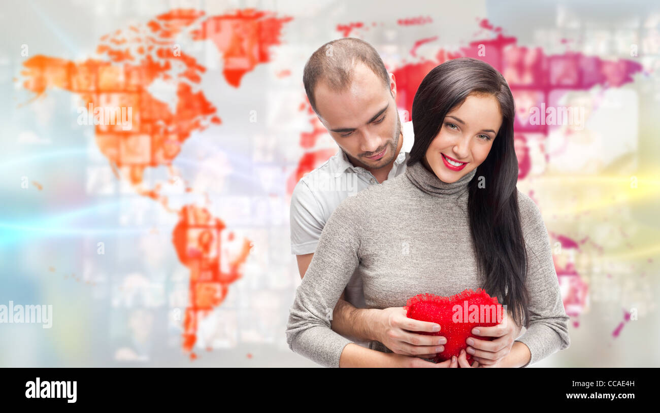 Porträt des jungen Paares umarmen und halten rotes Herz. Stehend vor Weltkarte mit Foto von Menschen. Internationale Partnersuche Stockfoto