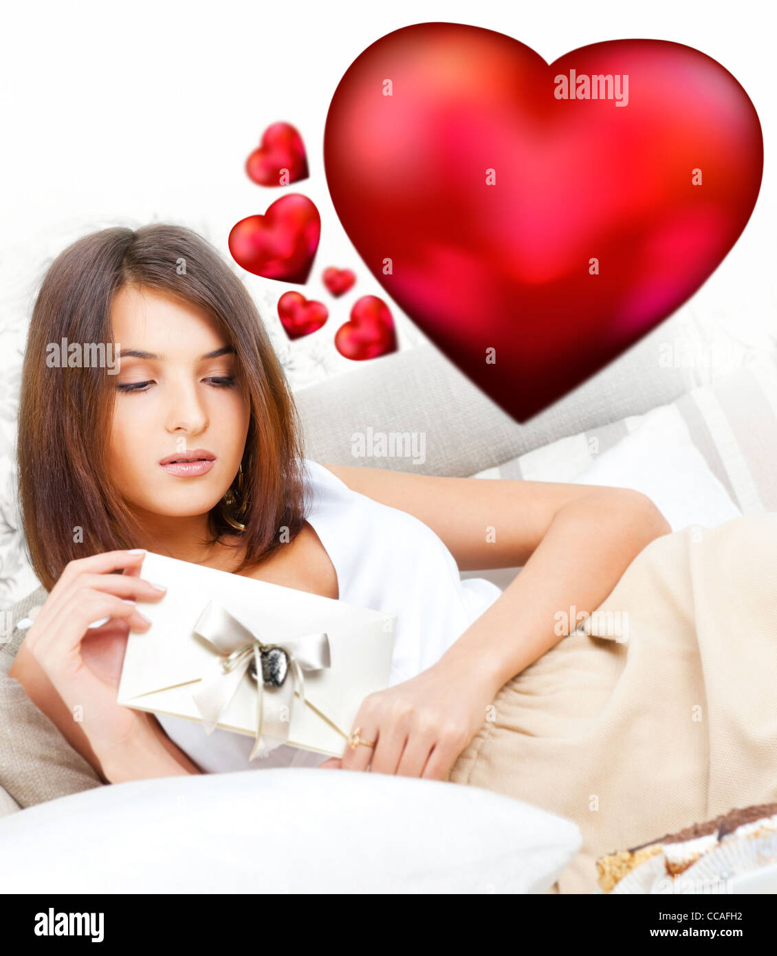Nette junge Frau hält einen Valentine und lesen. Wunderschönes Herz Symbole fliegen um sie herum. Sie ist verliebt in ihre paar Stockfoto