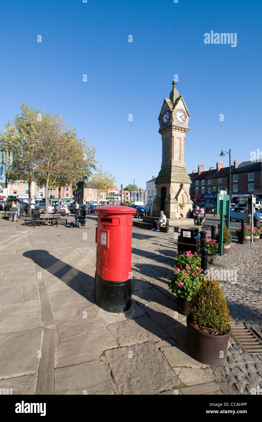 Ein roter Briefkasten und die Marktuhr im Zentrum der Marktstadt Thirsk in North Yorkshire, Großbritannien Stockfoto