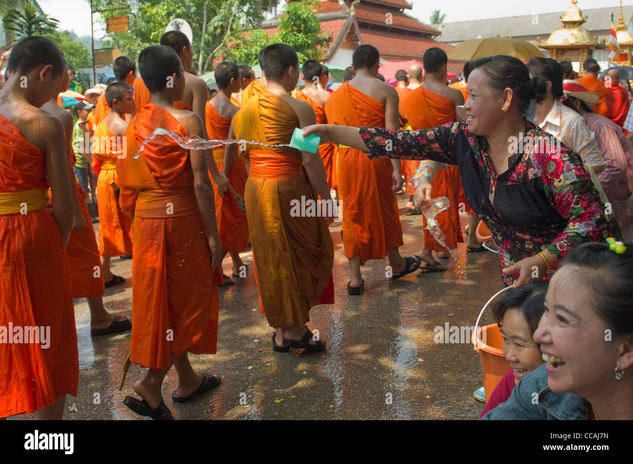 Lächelnd Lao Frauen werfen Wasser bei der Verarbeitung von buddhistischen Mönchen für einen Segen auf Mue Nau, der mittlere Tag der Lao Neujahr (Pi Mai Lao), Luang Prabang, Laos Stockfoto