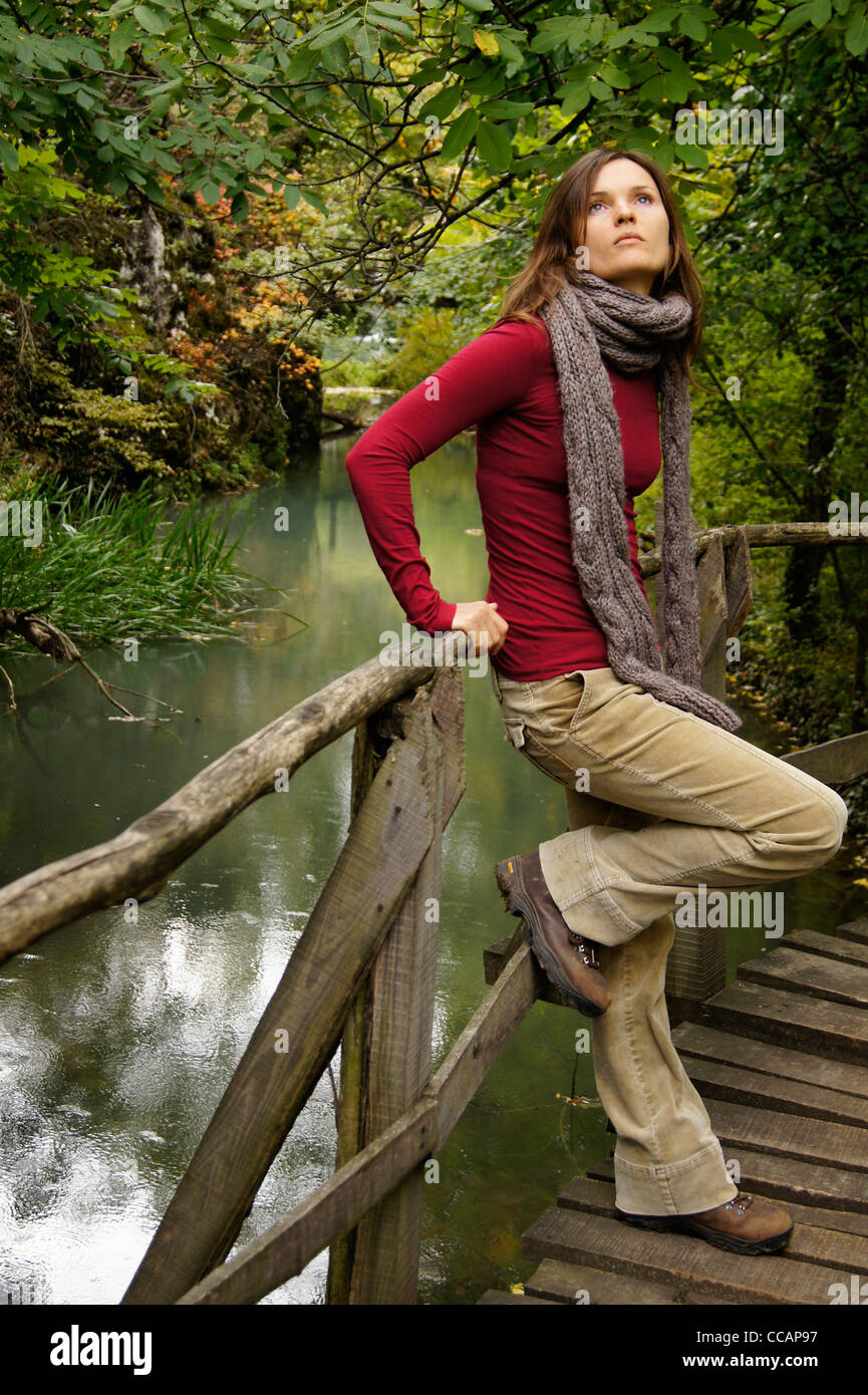 Schöne junge Frau, die Betrachtung des Himmels umgeben von üppiger grüner Vegetation, stützte sich auf eine Holzbrücke über einen noch See Stockfoto