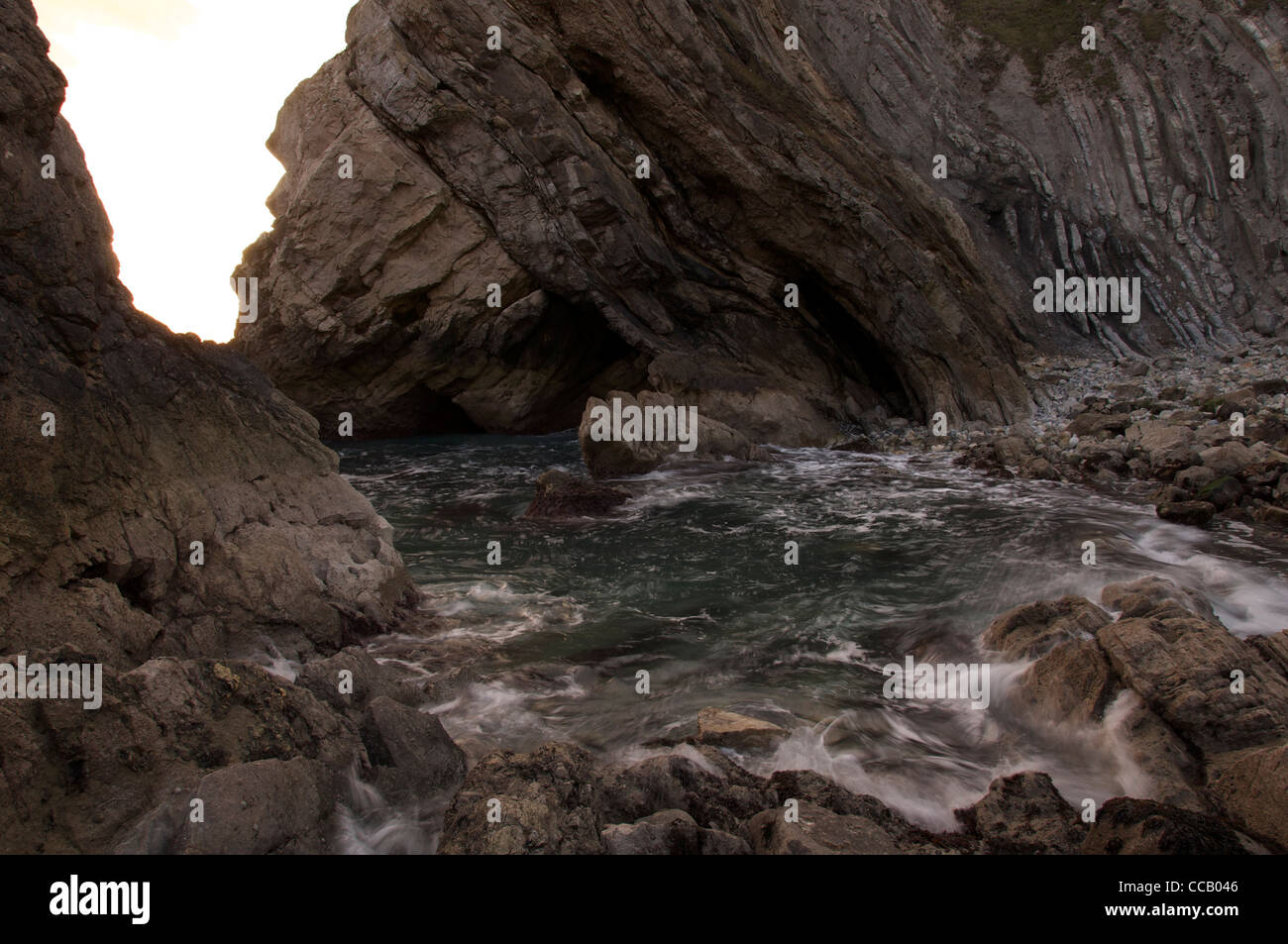 Wellen-Welle durch eine felsige Bucht in Stair Hole. Die geneigten Gesteinsschichten des "Lulworth Crumple" entnehmen bitte der Klippe hinter. Dorset, England, Vereinigtes Königreich. Stockfoto