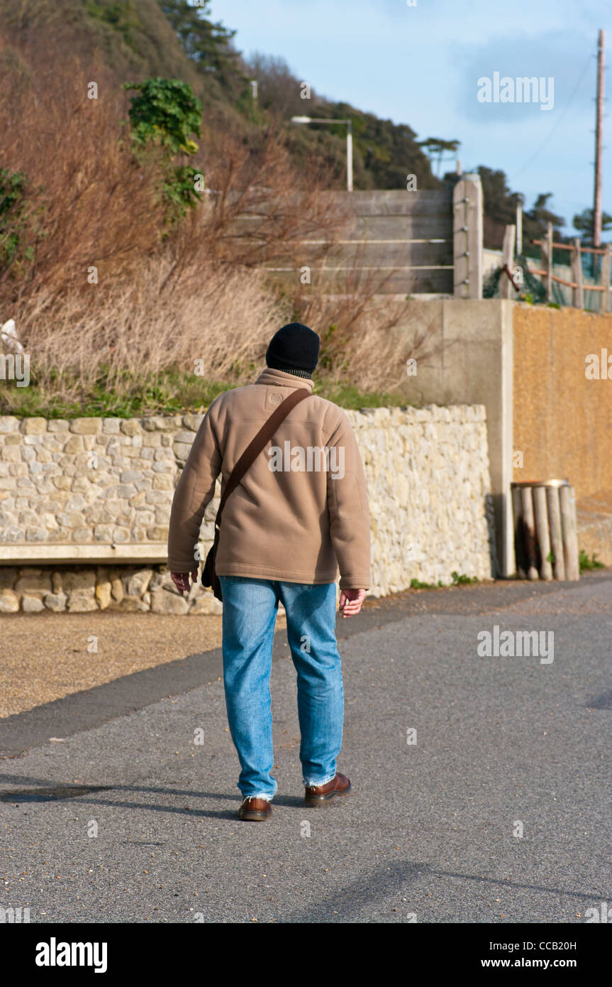 Rückansicht des ein Mann zu Fuß, ein Wintermantel Jacke Bluejeans und eine Wollmütze Stockfoto