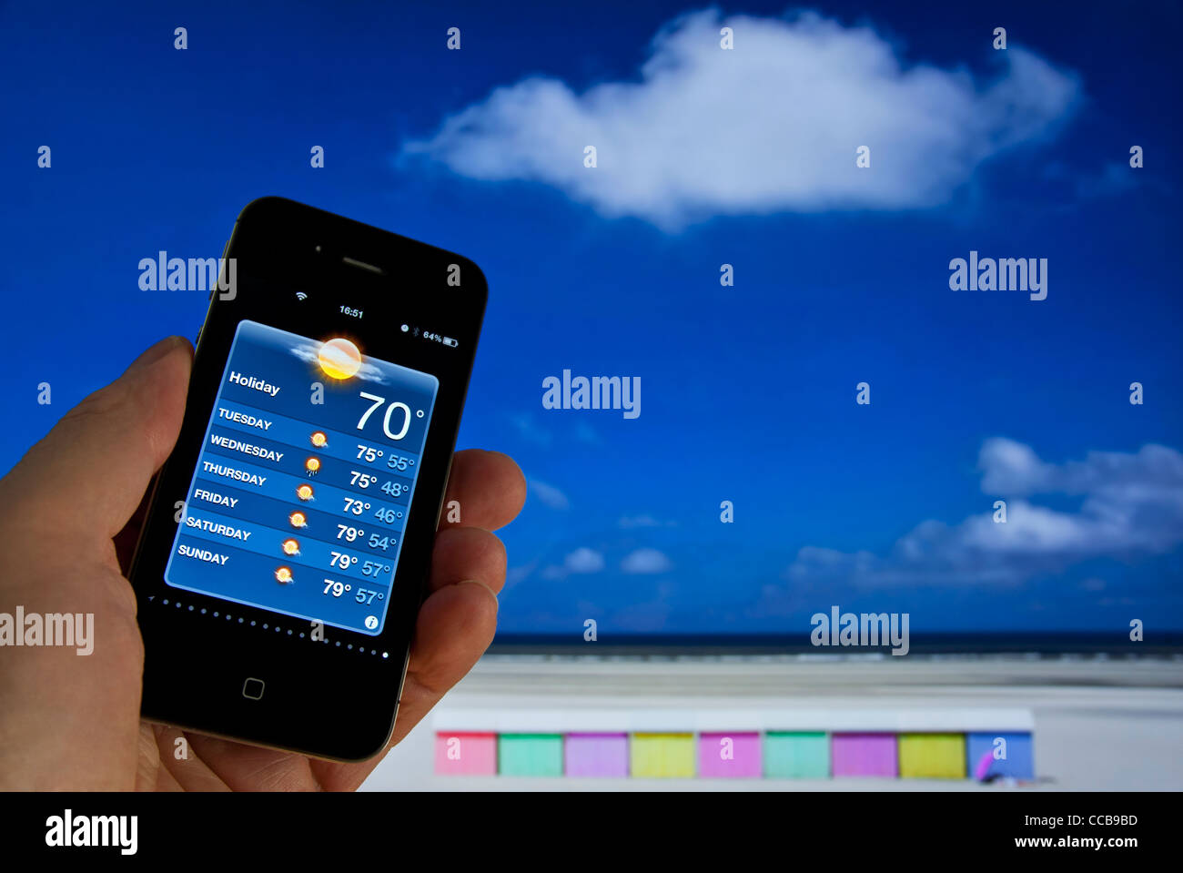 Hand, die Apple iPhone 4 s Woche "Urlaub" Sonne auf Wetter Smartphone Anwendung Strandhütten und Meer hinter anzeigen Stockfoto