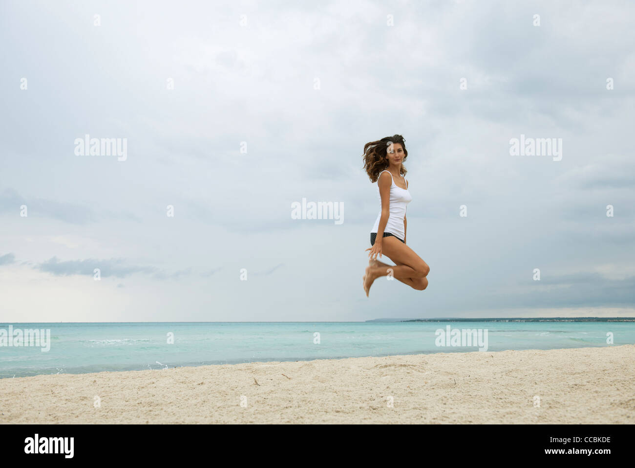 Junge Frau am Strand in die Luft springen Stockfoto