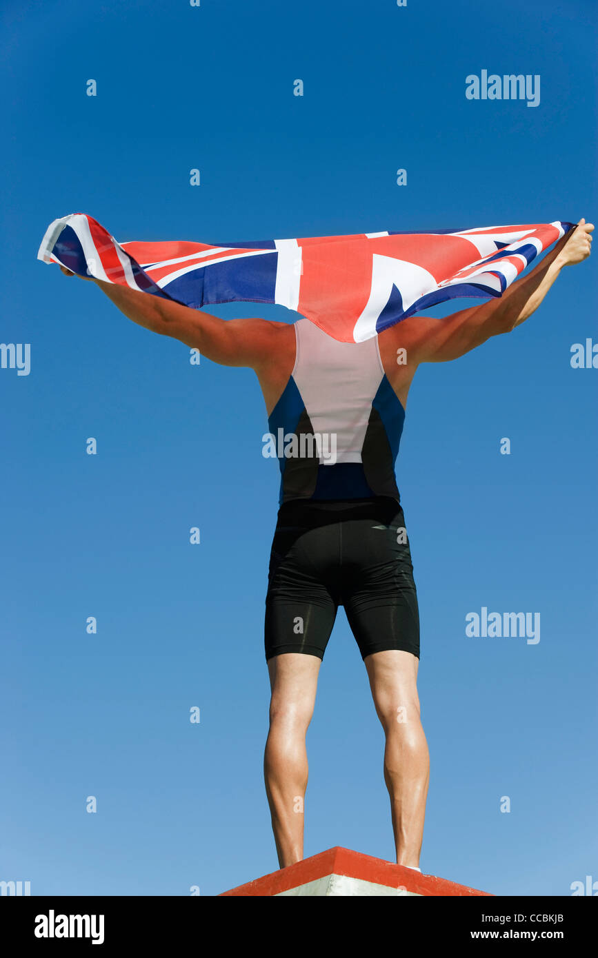 Männlicher Athlet auf Podest, hochhalten britische Flagge, Rückansicht Stockfoto