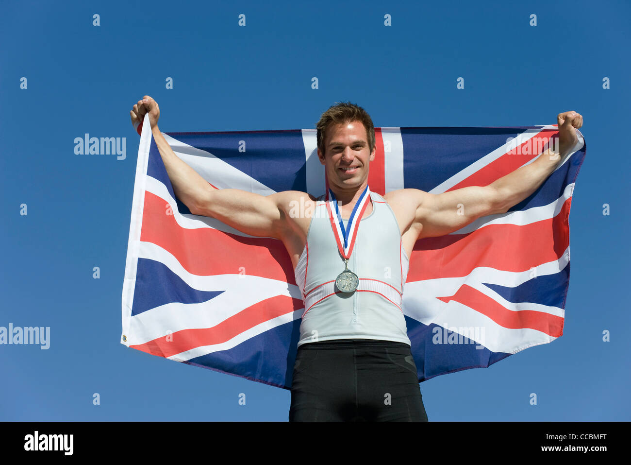 Männlicher Athlet auf Siegertreppchen, britische Fahne hochhalten Stockfoto