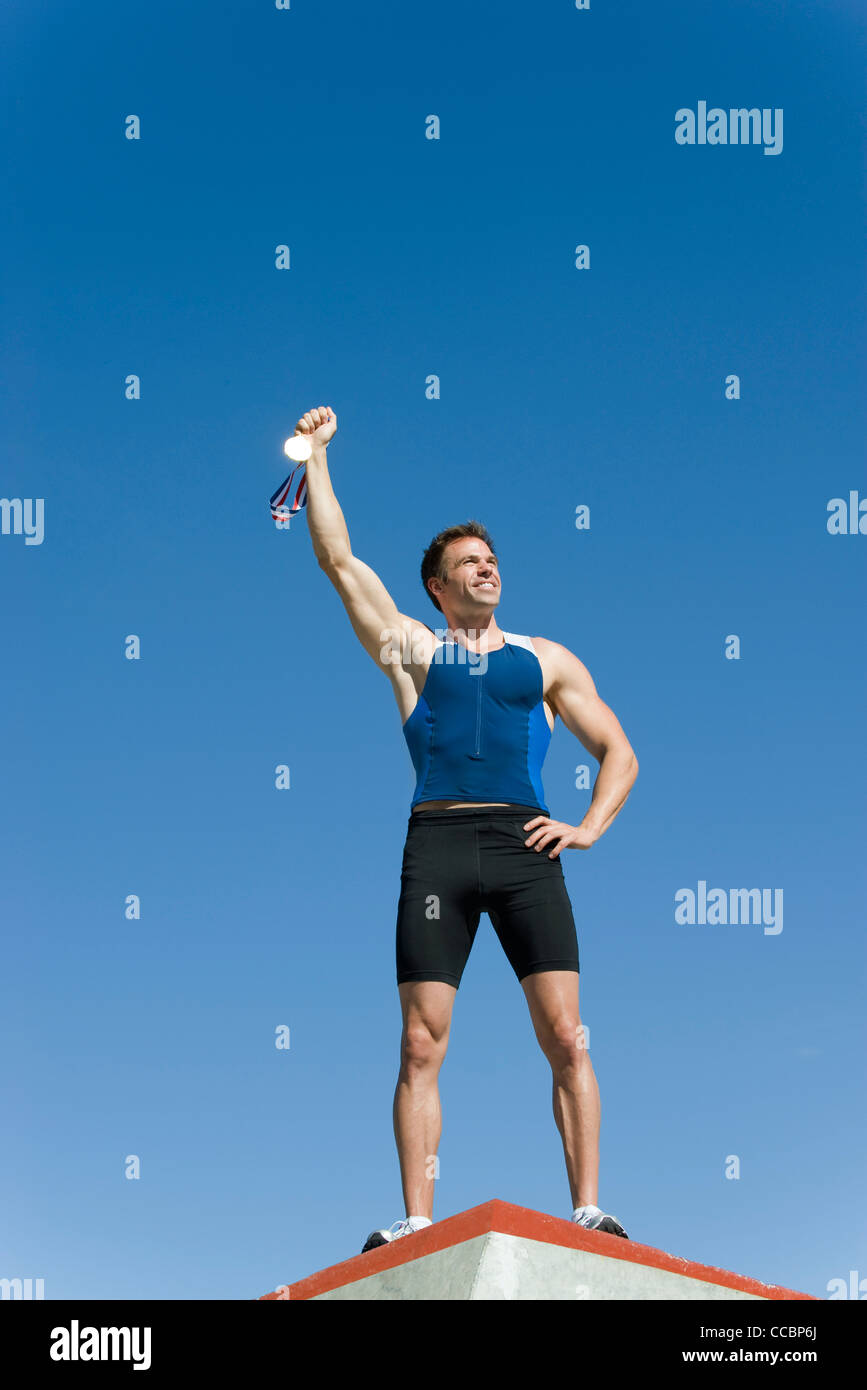 Männlicher Athlet auf Podest, Goldmedaille hochhalten Stockfoto