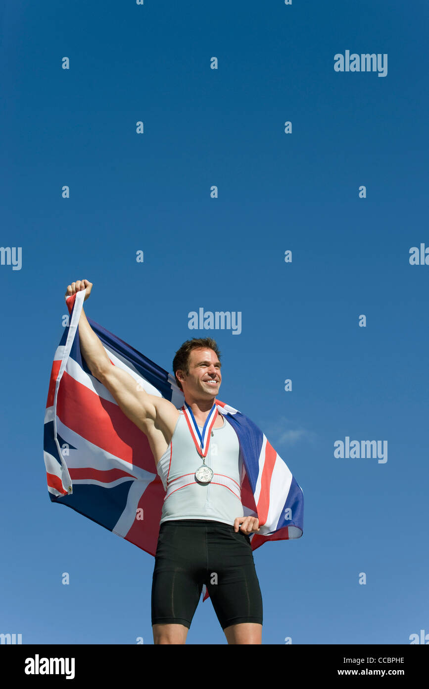 Männlicher Athlet auf Siegertreppchen, britische Fahne hochhalten Stockfoto