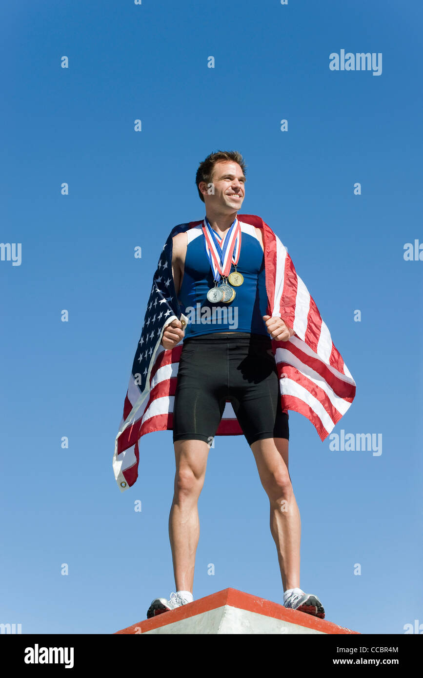 Männlicher Athlet auf Siegertreppchen, eingewickelt in amerikanische Flagge Stockfoto