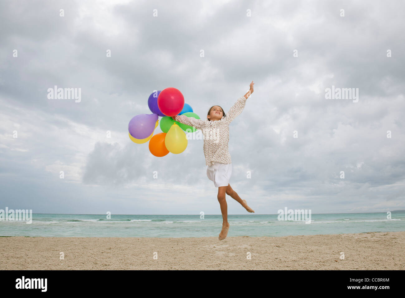 Mädchen am Strand mit Haufen von bunten Luftballons springen Stockfoto