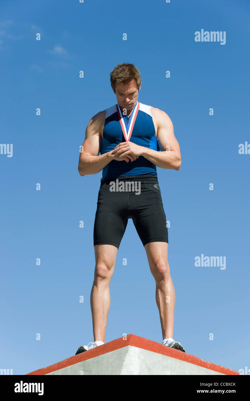 Männlicher Athlet auf Siegertreppchen, Medaille halten und nach unten Stockfoto