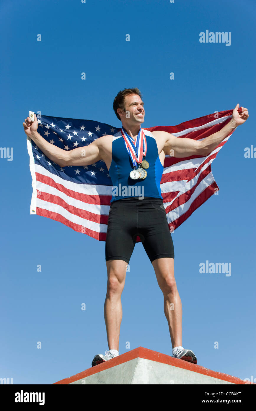 Männlicher Athlet auf Siegertreppchen, amerikanische Fahne hochhalten Stockfoto