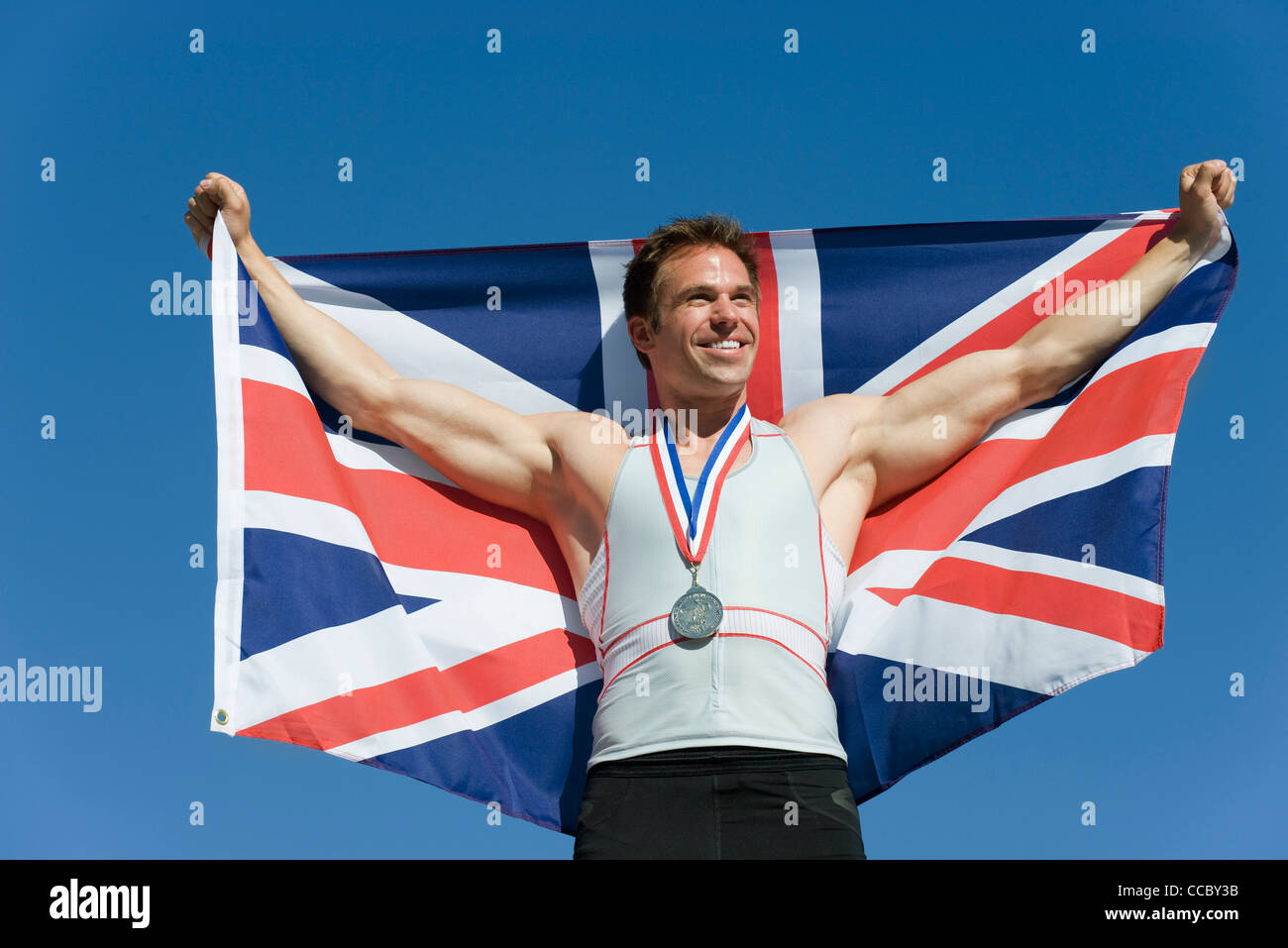 Männlicher Athlet auf Siegertreppchen, britische Fahne hochhalten Stockfoto