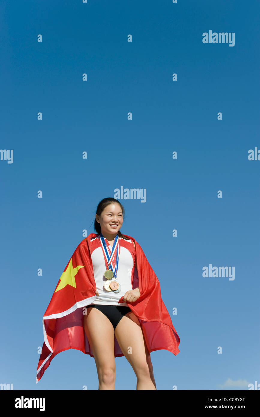 Sportlerin auf Siegertreppchen, eingehüllt in chinesische Flagge Stockfoto