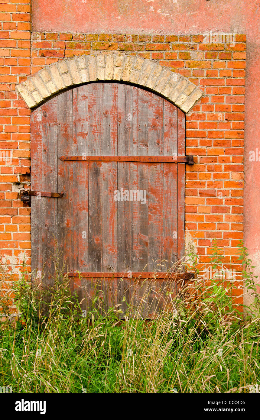 Alter verlassenen Bauernhof Gebäude Türen mit Schloss und hohe Gräser gesperrt. Aus rotem Backstein-Gebäude-Hintergrund. Stockfoto