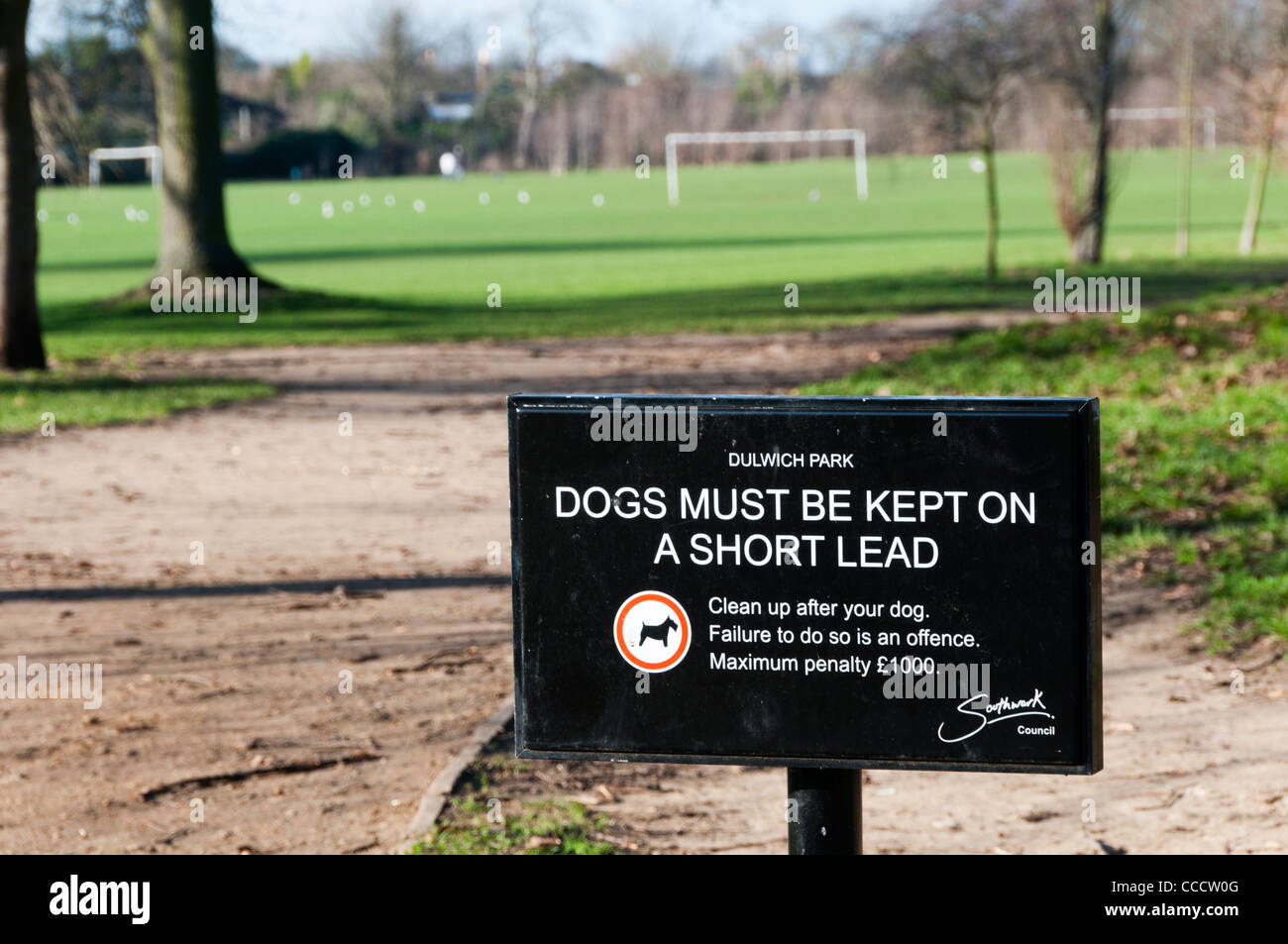 Ein Schild sagt Eigentümer halten Hunde an der Leine und Aufräumen nach ihnen mit aus Fokus Spielfelder im Hintergrund. Stockfoto