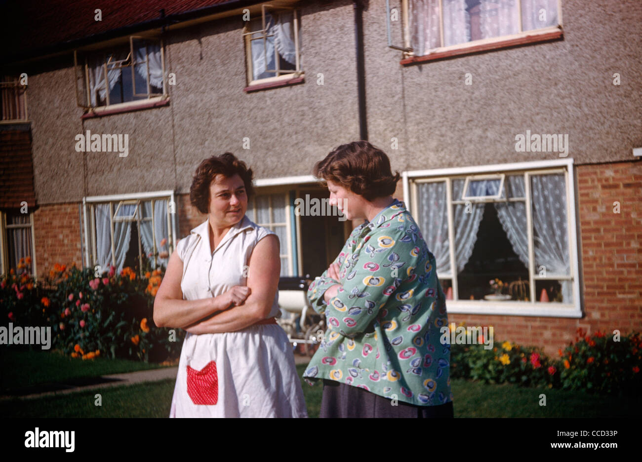 Zwei Mütter und Nachbarn Klatsch mit Armen gefaltet vor ihren Häusern auf einem Grundstück von Essex in den frühen sechziger Jahren. Stockfoto