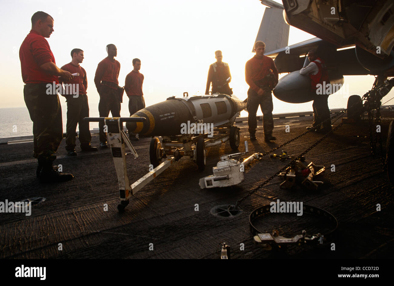 Rote Hemden Ordnance Männer bereiten und intelligente Bomben zu einer F/A-18 Kampfjet auf dem Deck der USS Harry S Truman passen. Stockfoto