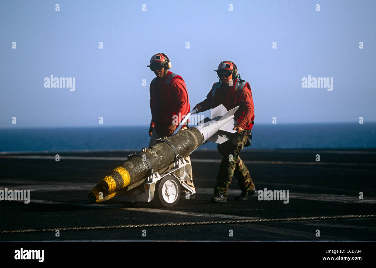 Rote Hemden Ordnance Männer bereiten, intelligente Bomben zu einer F/A-18 Kampfjet auf dem Deck der USS Harry S Truman passen. Stockfoto