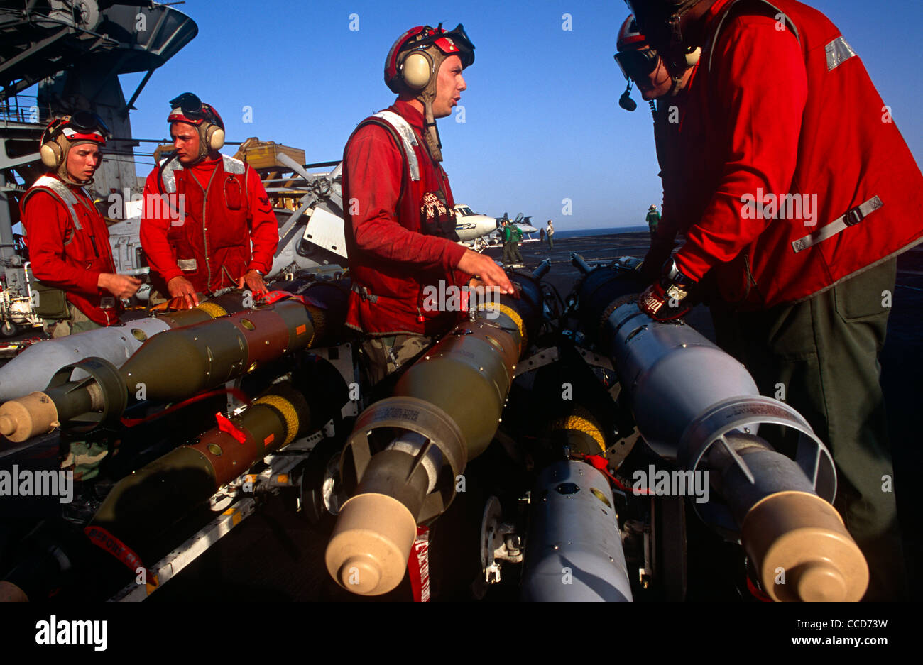 Rote Hemden Ordnance Männer bereiten Sie intelligente Bomben und Raketen, die eine F/A-18 Kampfjet auf dem Deck der USS Harry S Truman passen. Stockfoto