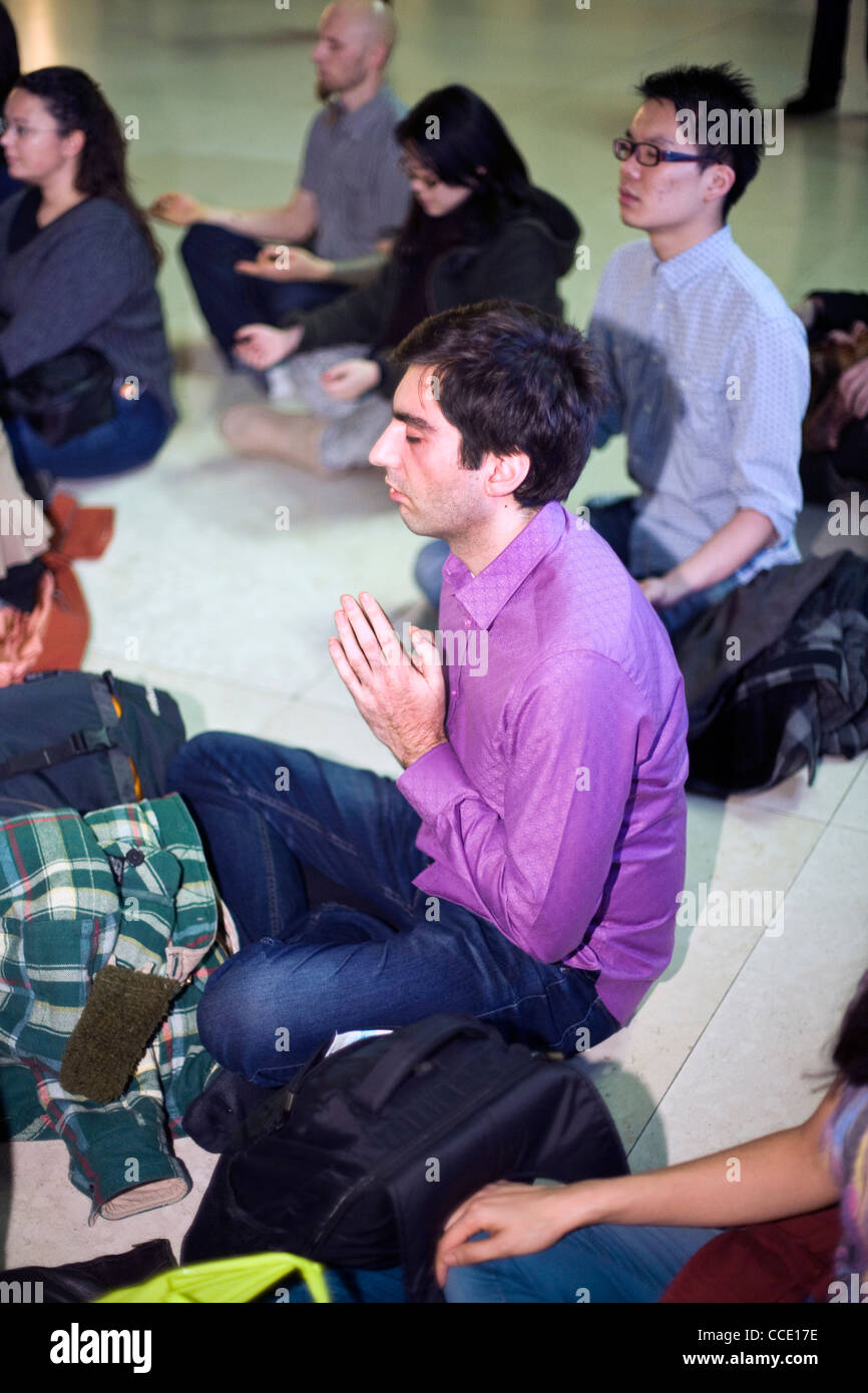 Ein Mann meditiert im Hintergrund als Teil einer Meditation-Flashmob in der Great Court des British Museum Stockfoto
