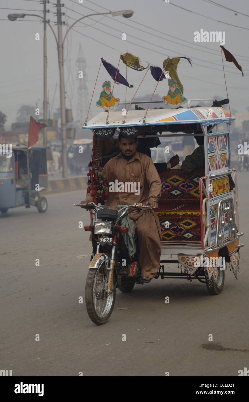 Eine Motorrad-Rikscha dekoriert mit ständig nicken Flaggen summt durch Staub und Dunst des Verkehrs von Lahore in Pakistan. Stockfoto