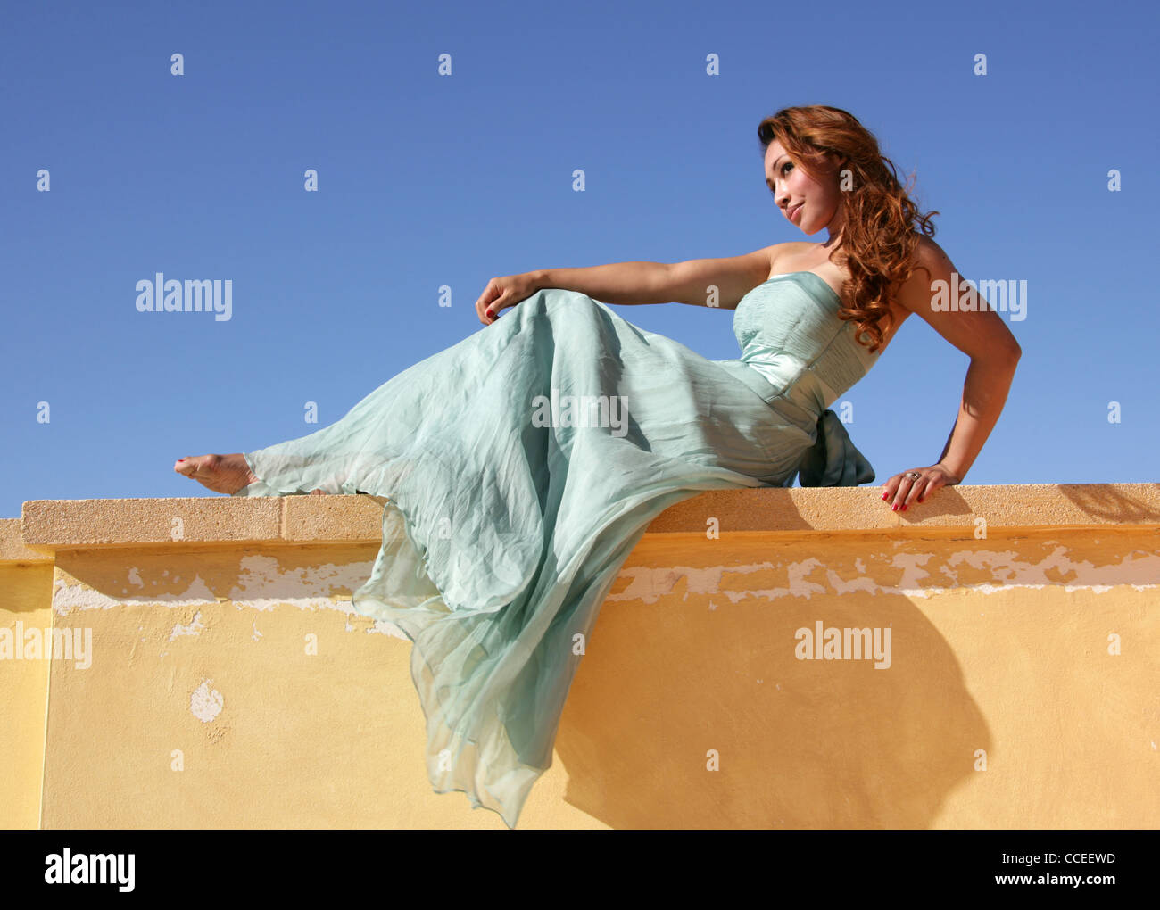 Indonesierin in einem Türkis Kleid Verlegung auf eine gelbe Wand, Fuerteventura, Kanarische Inseln, Spanien. Stockfoto