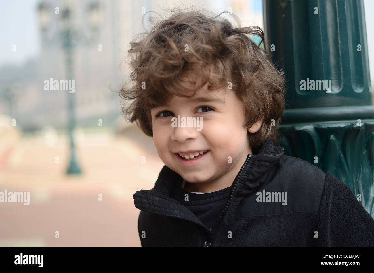 Ein hübscher kleiner Junge lehnt sich an gegen einen Lichtmast und lächelt in die Kamera. Stockfoto