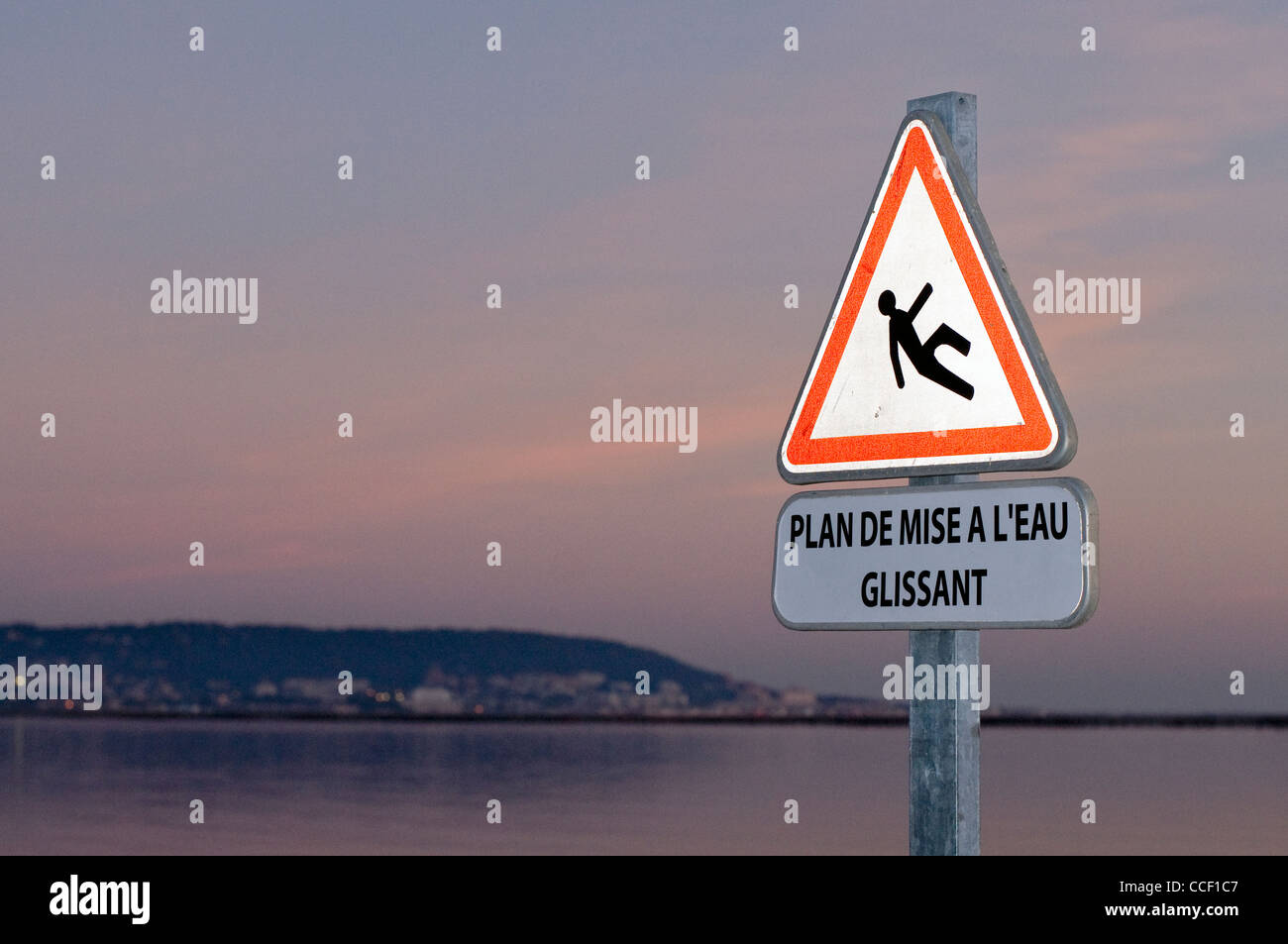 Rutschige Oberfläche Zeichen (auf Französisch) gegen Blick auf See. Stockfoto