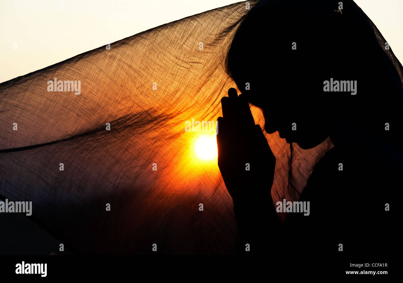 Indische Teenager-Mädchen beten bei Sonnenuntergang mit einem Schleier bedeckt. Silhouette. Indien Stockfoto