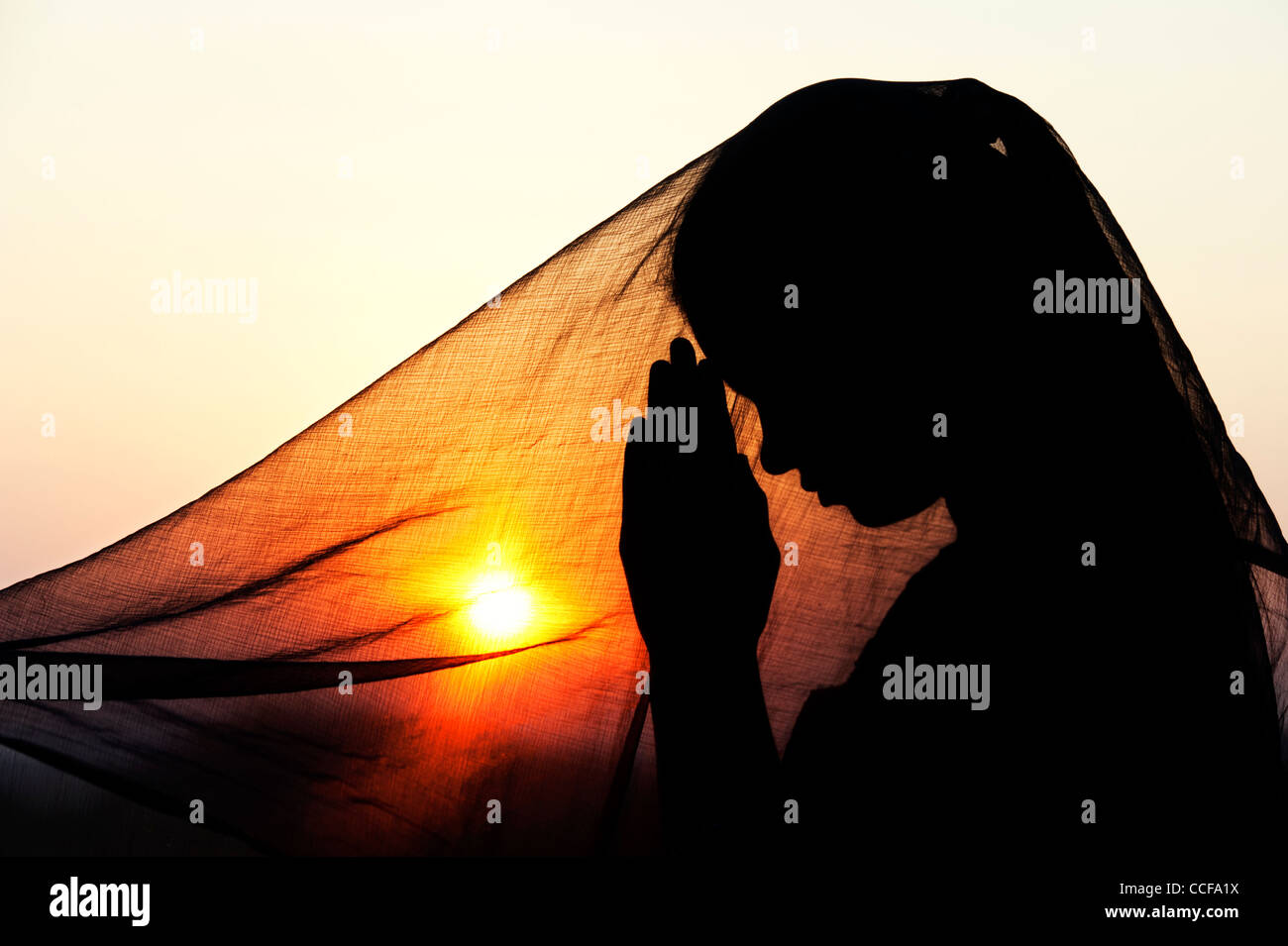 Indische Teenager-Mädchen beten bei Sonnenuntergang mit einem Schleier bedeckt. Silhouette. Indien Stockfoto
