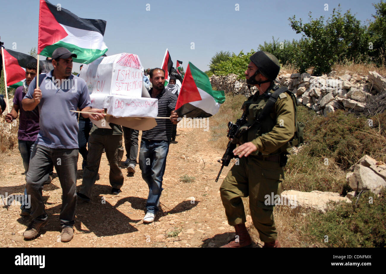 Israelische Soldaten bewachen, als Demonstranten palästinensische Flagge während einer Demonstration von ausländischen, israelischen und palästinensischen Aktivisten gegen die jüdische Ansiedlung Karmei Tzur in der Nähe von palästinensischen Dorf Beit Omar in der südlichen Westbank-Stadt Hebron am 4. Juni 2011 halten. Foto: Naj Stockfoto