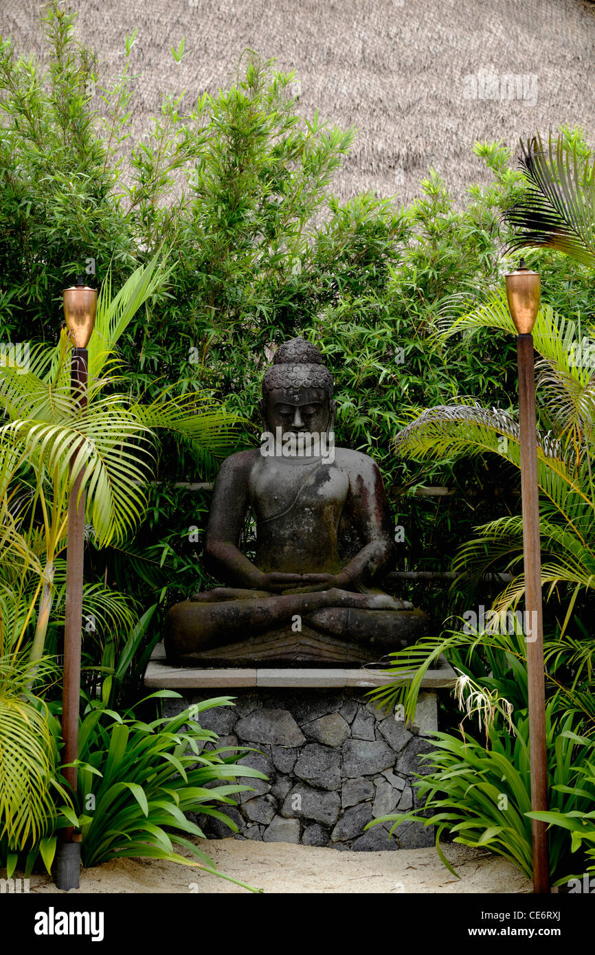 Stein Buddha umgeben von Bäumen mit Fackeln im Vordergrund Stockfoto